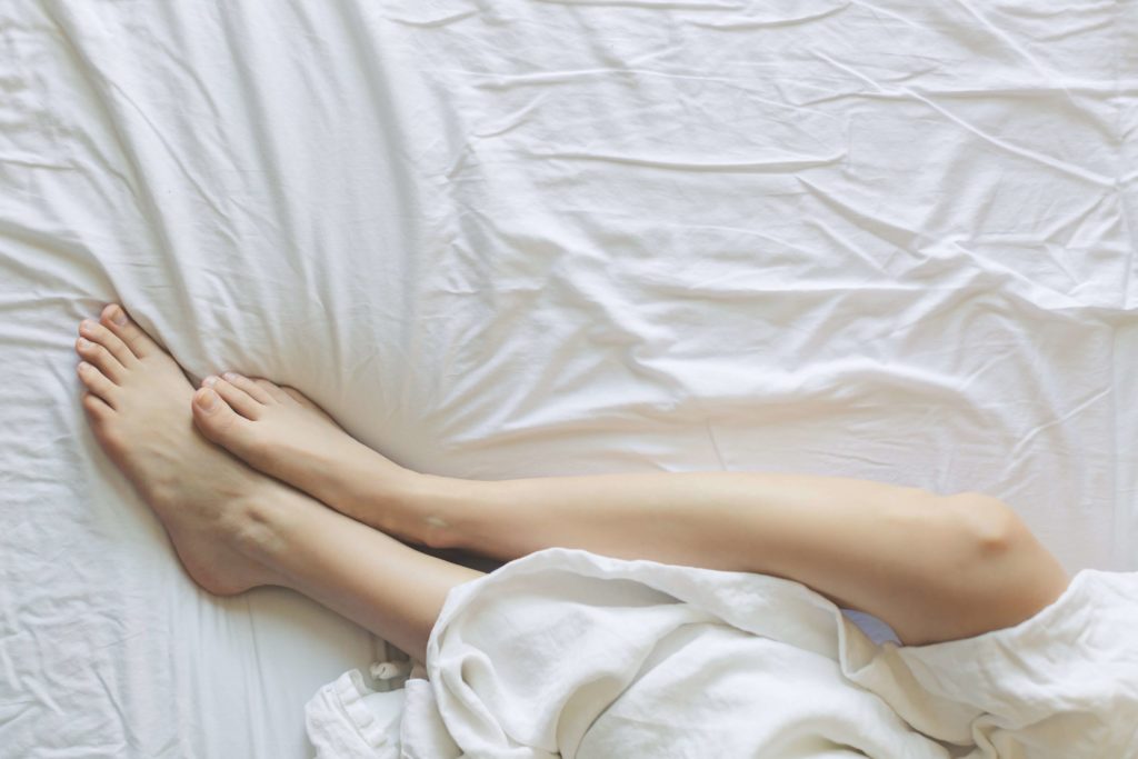 Cramping, sign of early pregnancy - woman's feet between sheets in bed