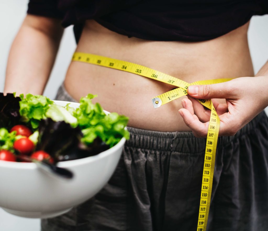 Nutrition during pregnancy should be tailored to gain weight but not too much - a woman measuring her waist and holding bowl of salad.